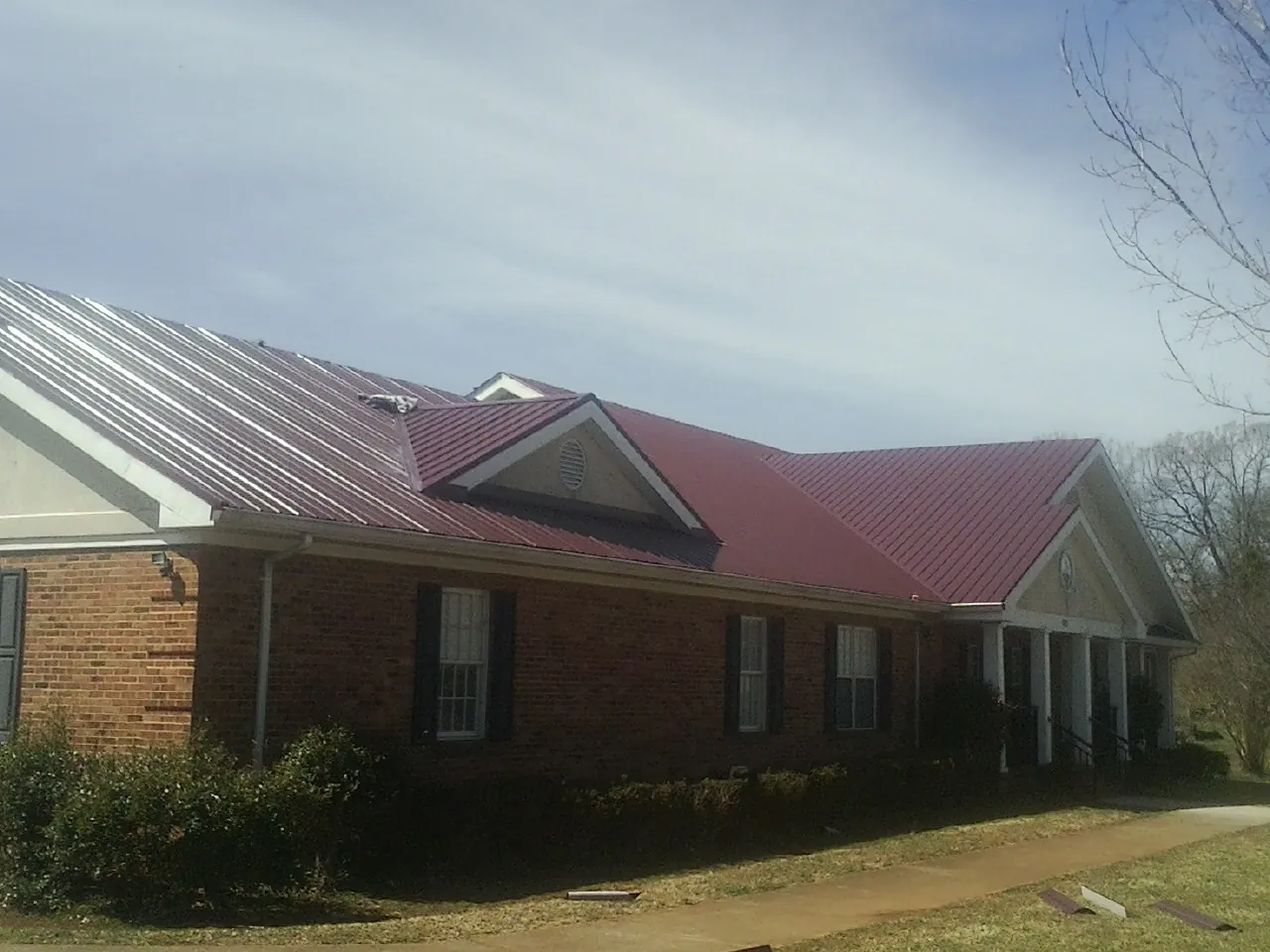 Red metal roof with gabled entries on a long brick building, from a Hail Damage Roof Repair job in Bethune