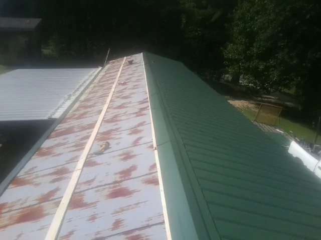 Old rusted panels beside newly installed green metal roofing — Wind Damage Roof Repair by Roofing Brothers in Bethune