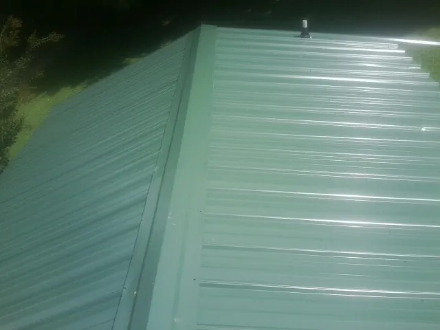 New green metal panels meeting at the ridge of a roof — Flat Roof Repair work by our crew in Bethune