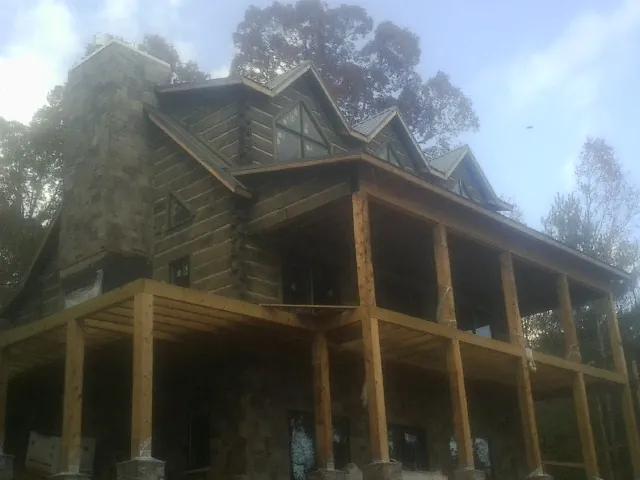 Stone chimney and dormers on a large log home with a timber porch in Bethune